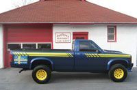 a blue truck with yellow wheels is parked in front of a white building