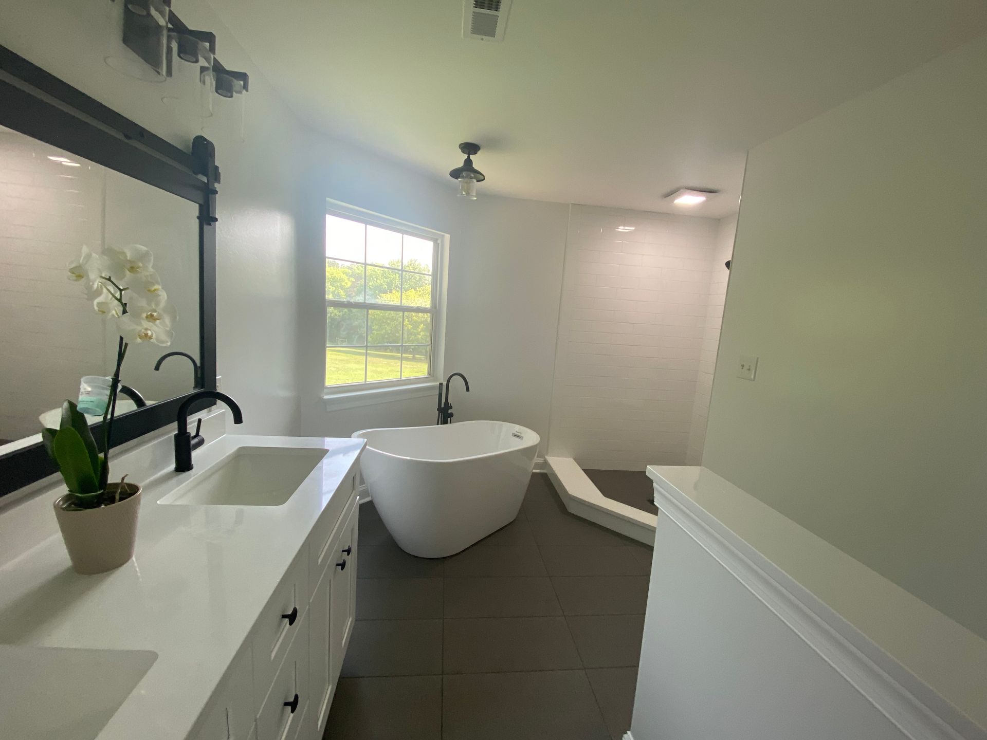 A bathroom with a tub , sink , mirror and window.