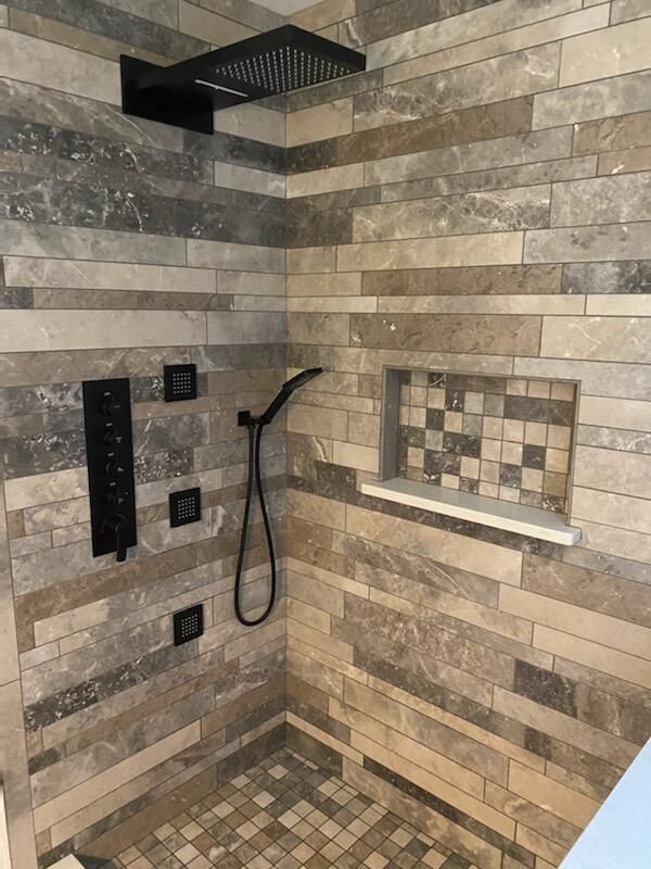 A shower with a tiled wall and a black shower head.