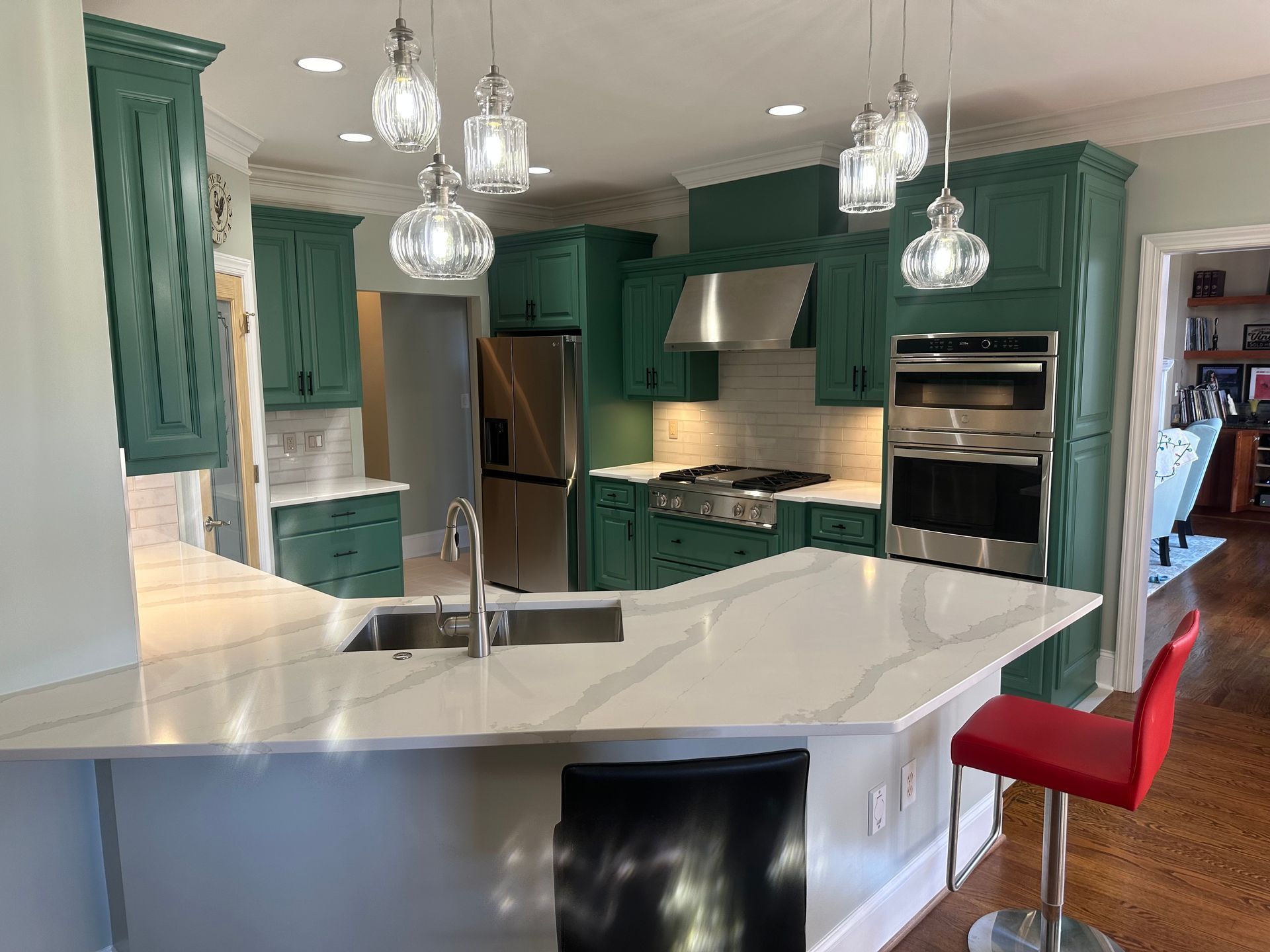 A kitchen with green cabinets , white counter tops , and stainless steel appliances.