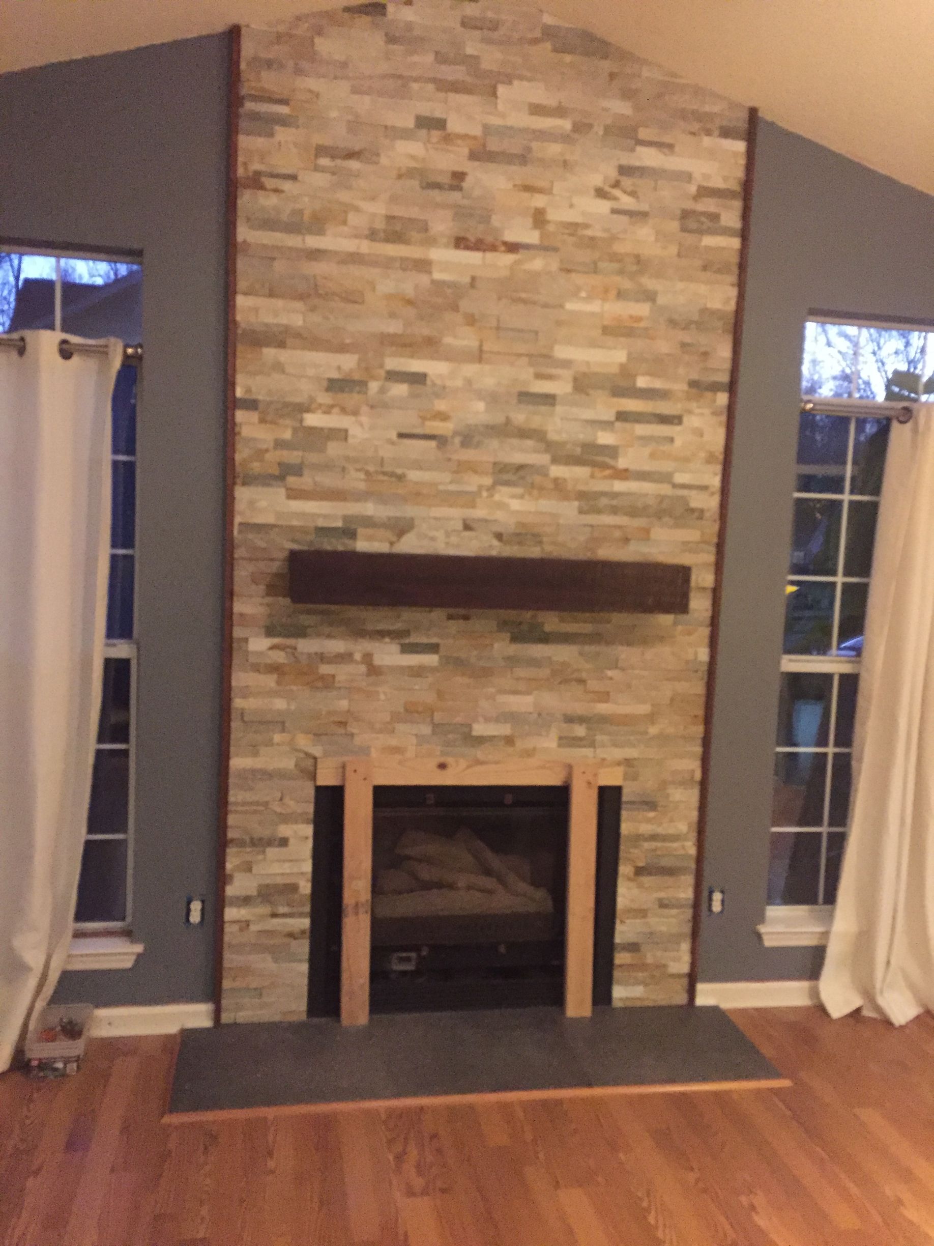 A living room with a stone fireplace and a wooden mantle.