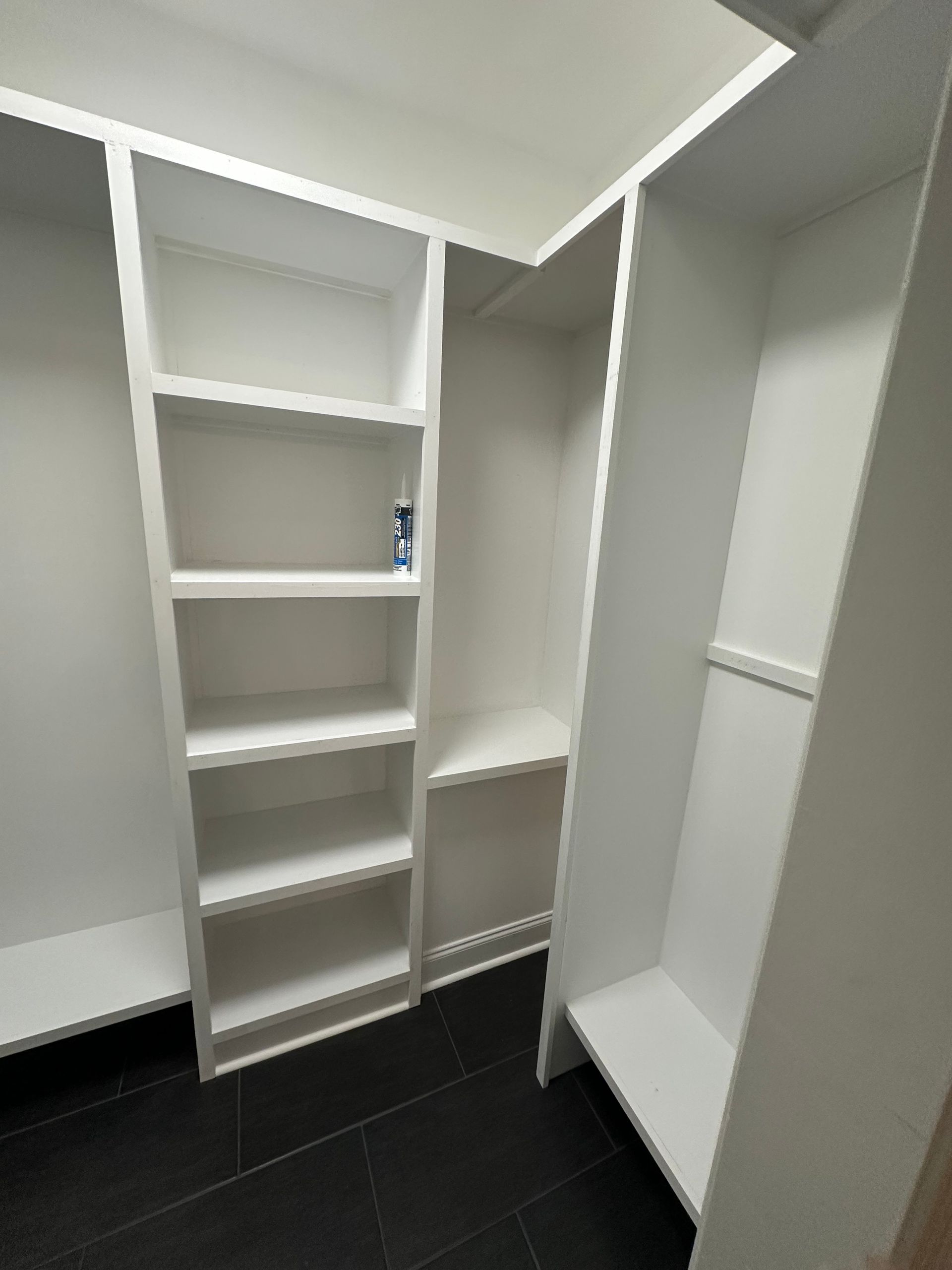 A walk in closet with white shelves and black tile floors.