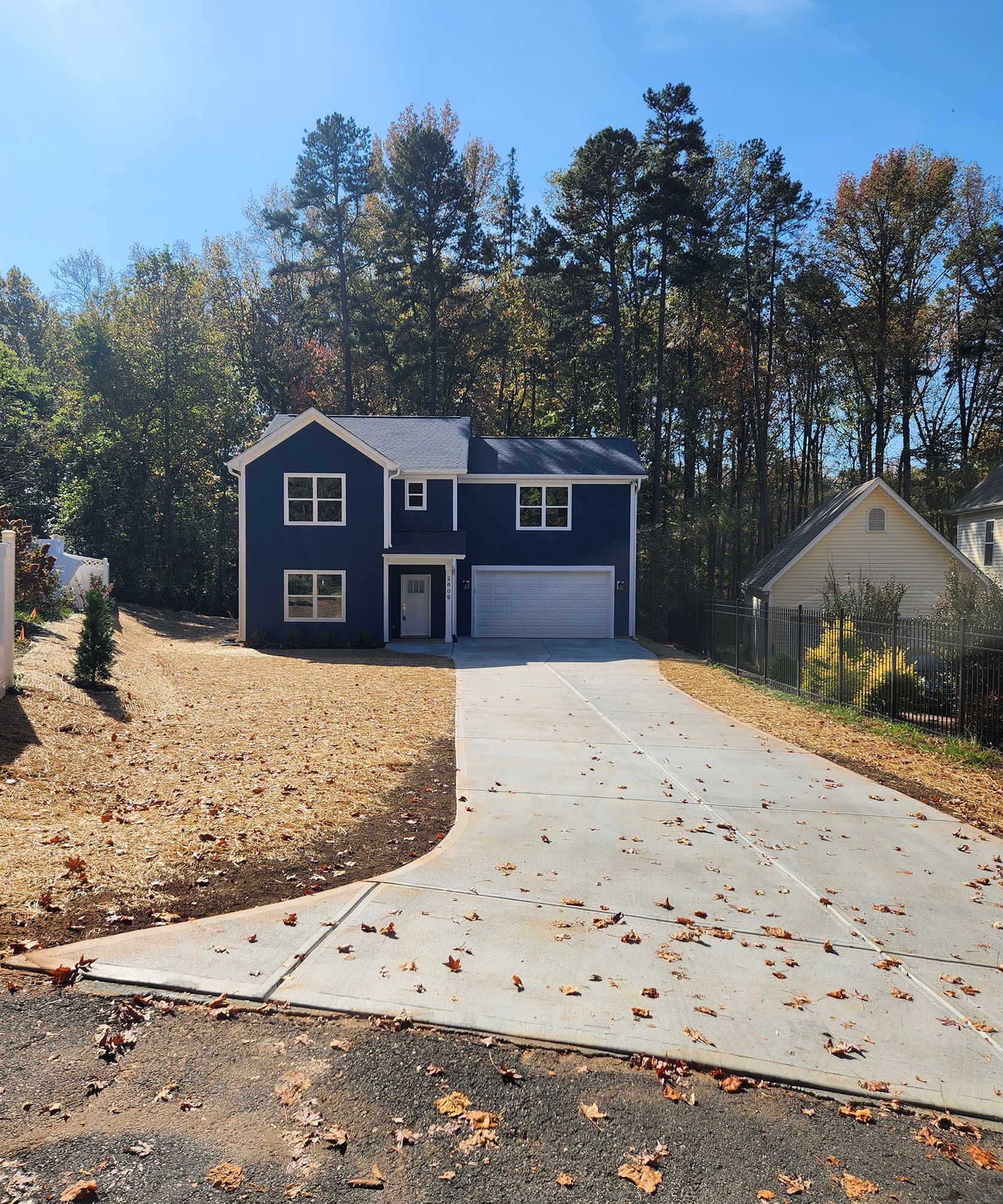 A blue house with a white garage door is surrounded by trees