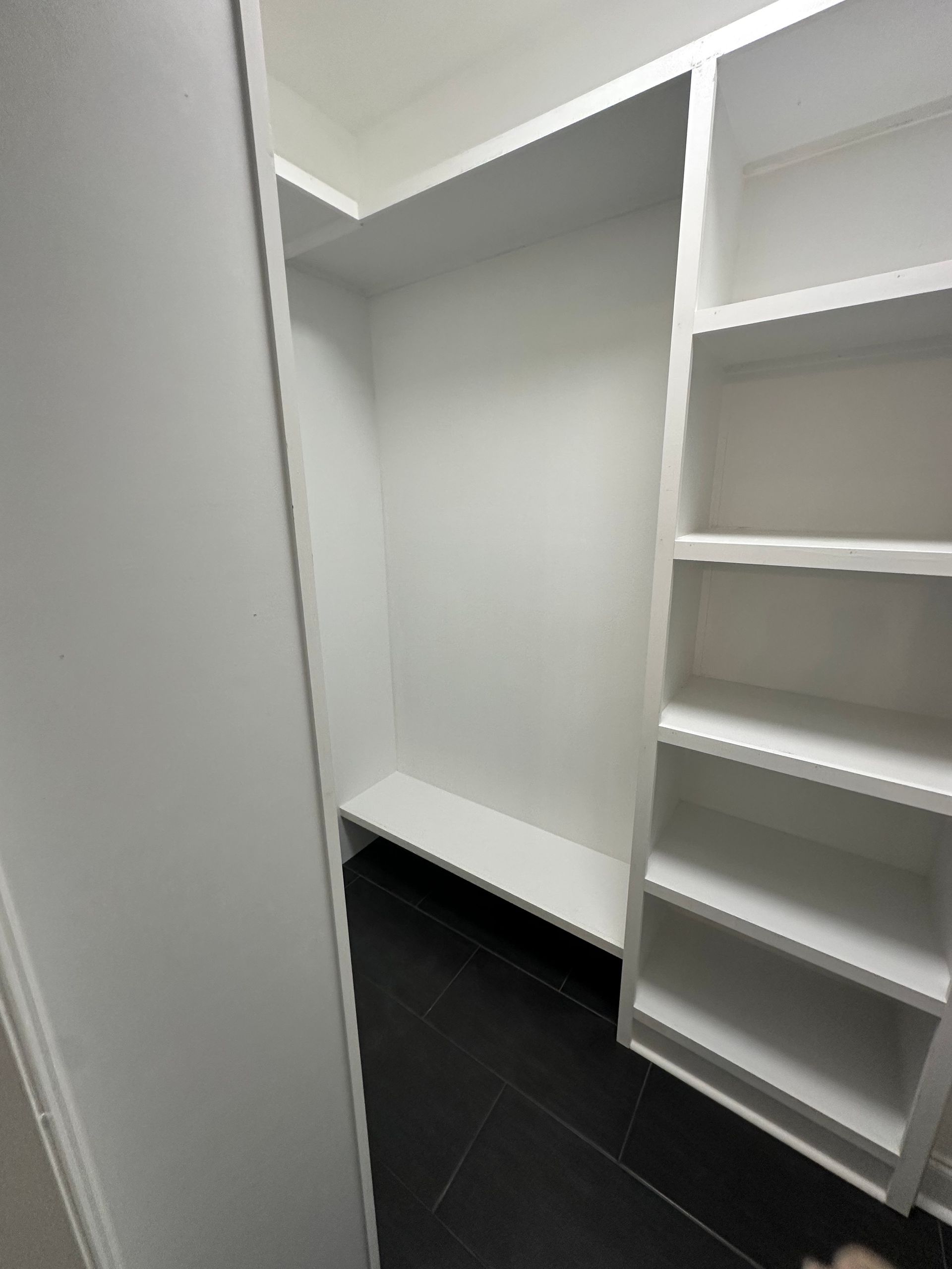 A walk in closet with white shelves and a bench.