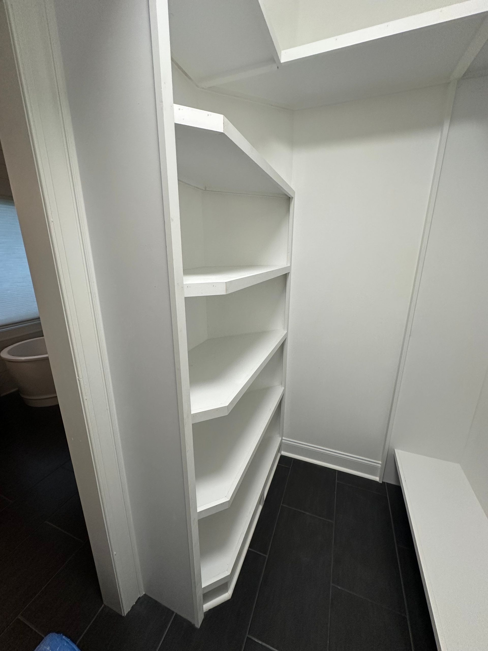 A walk in closet with white shelves and a black floor