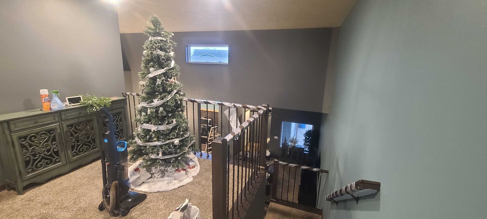 A christmas tree is sitting in the middle of a living room next to a staircase.