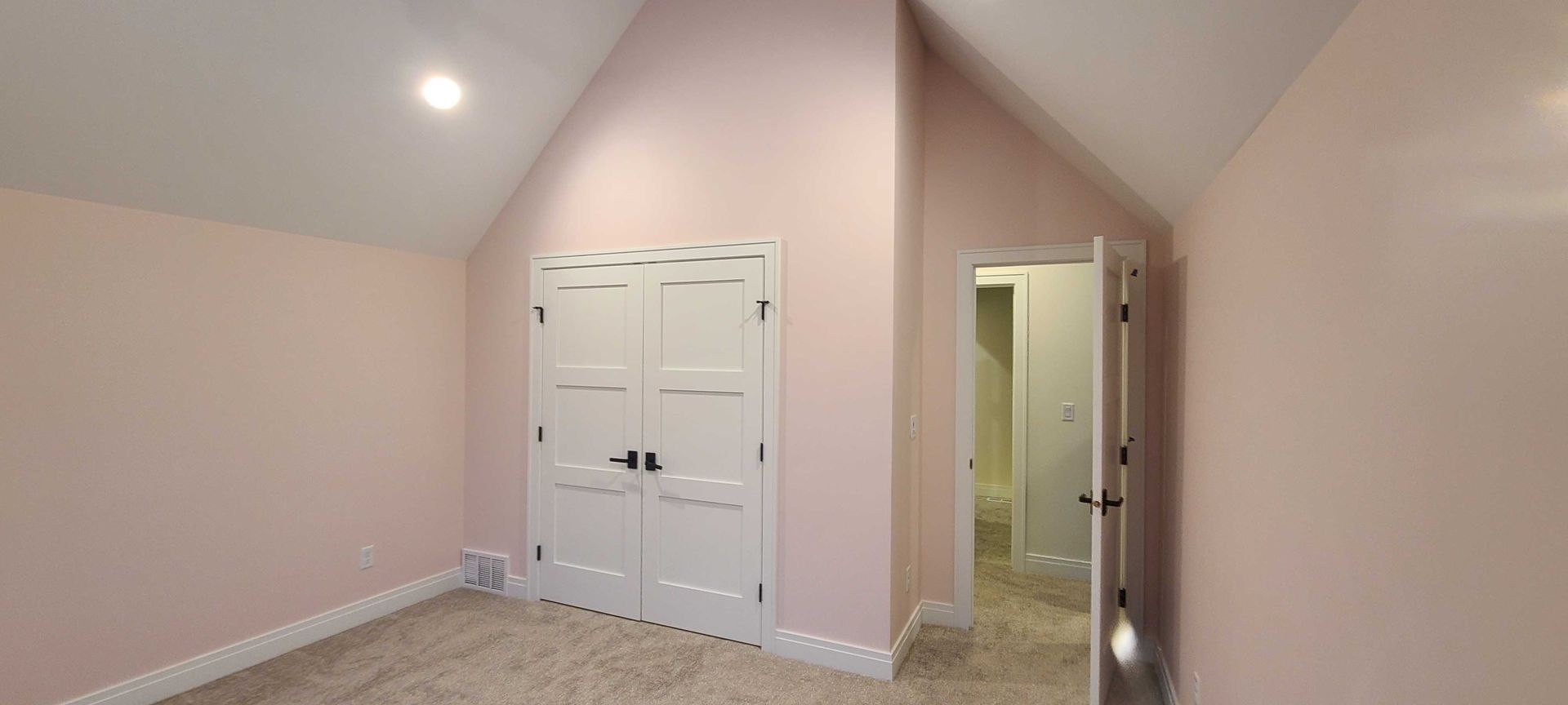 An empty room with pink walls and white doors and a vaulted ceiling.
