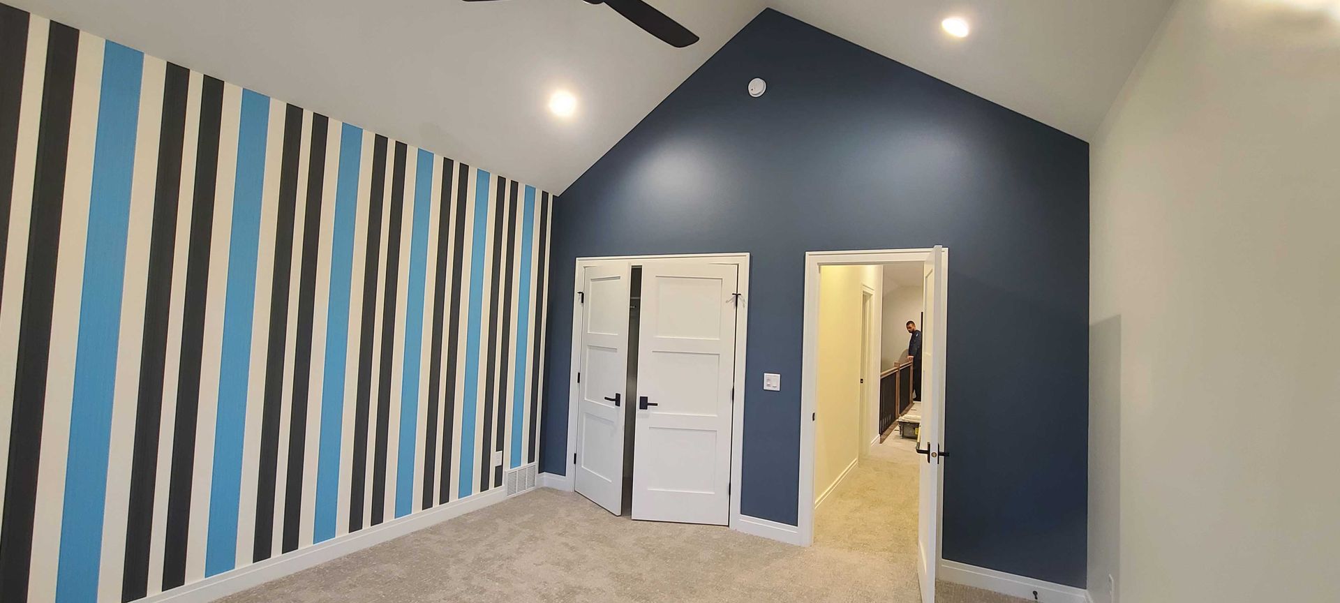 A room with blue and white stripes on the wall and a ceiling fan.