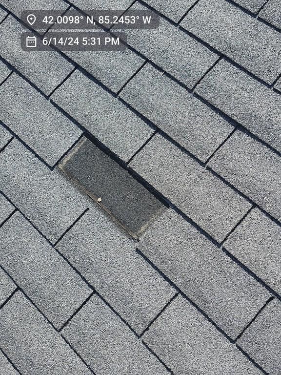 A roof section with gray asphalt shingles, featuring a single, missing or damaged rectangular shingle exposing the underlay.
