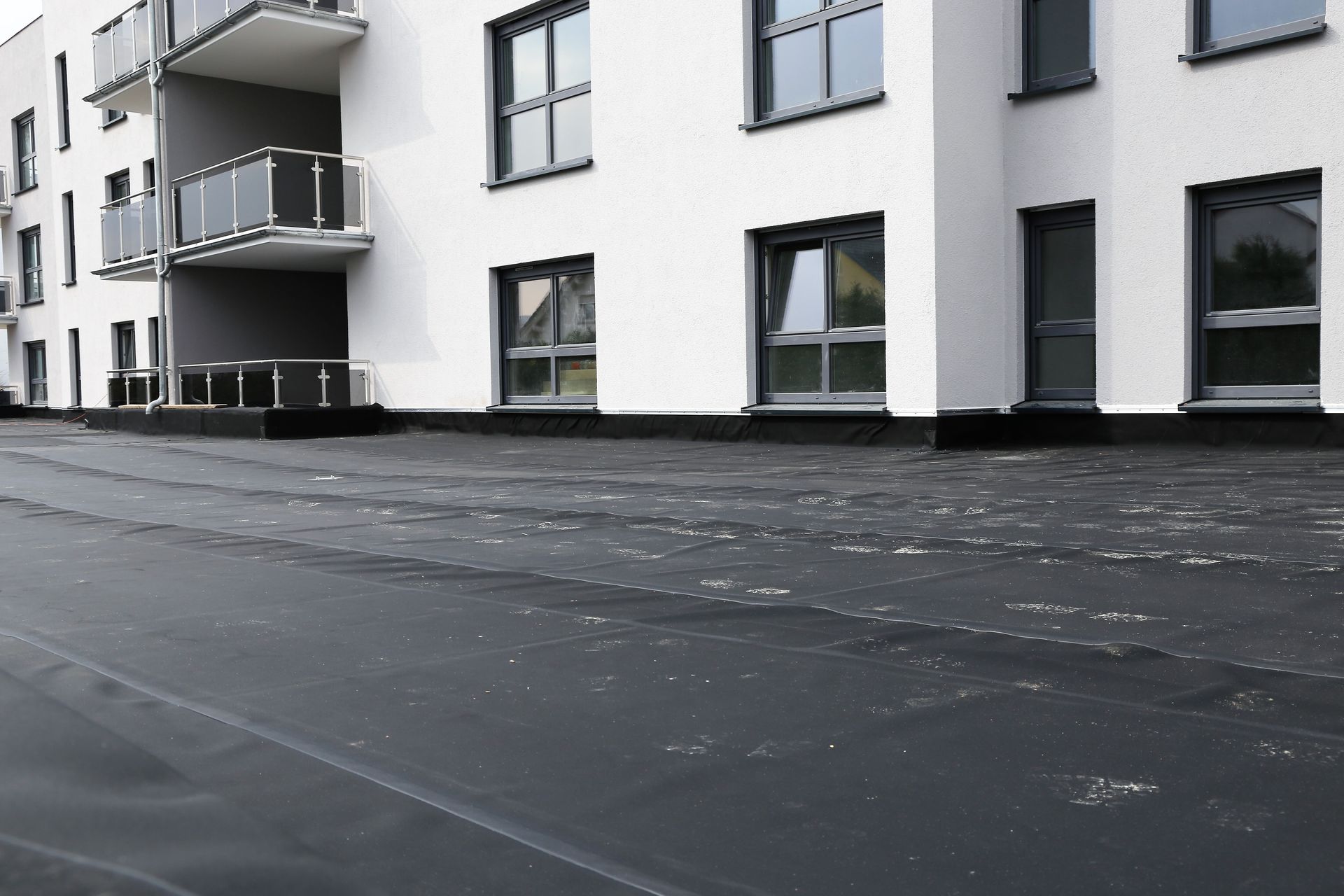 Black waterproofing membrane installed on the ground level of a modern white apartment building.