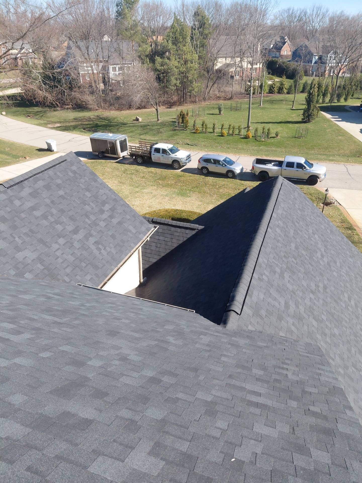 A view from a shingled roof looking down at a suburban street with three parked trucks and a trailer.