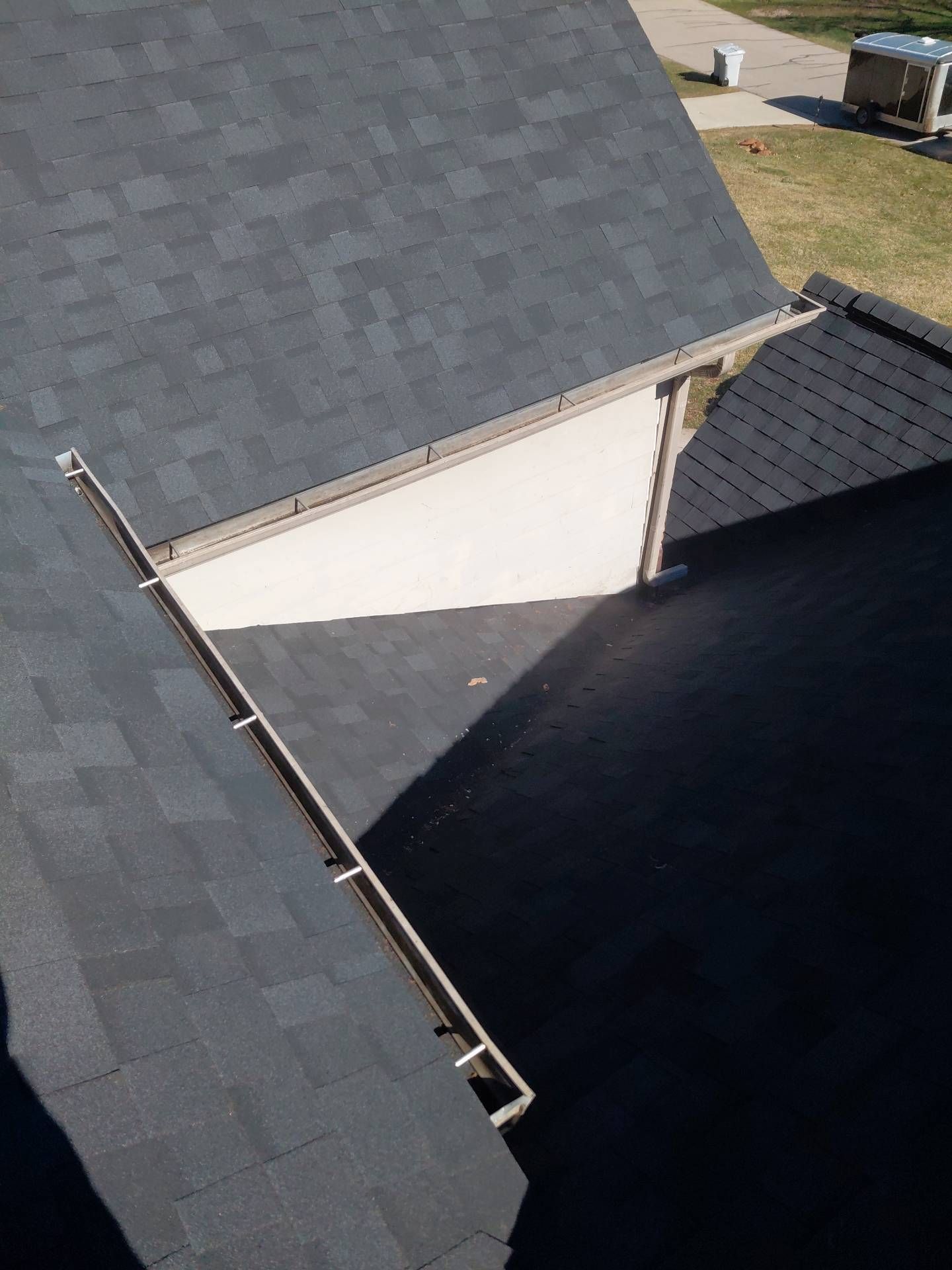 High-angle view of dark gray roof shingles and a white wall, featuring a roof valley with an installed gutter system.