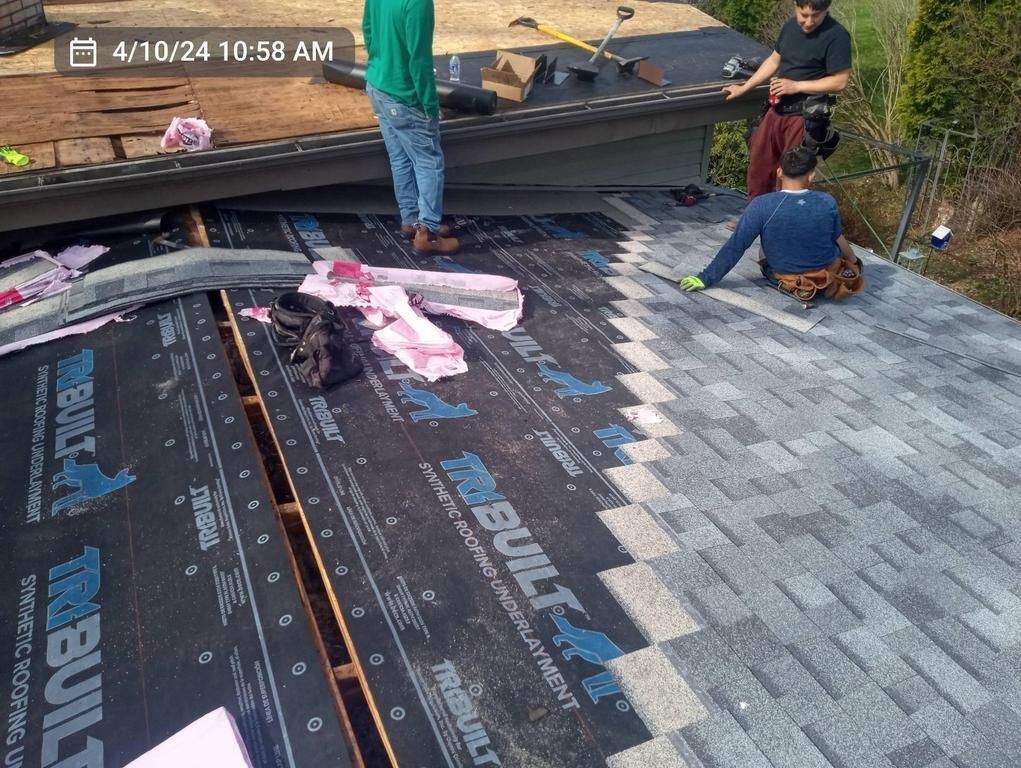 Three workers installing shingles on a sloped residential roof covered with black underlayment.