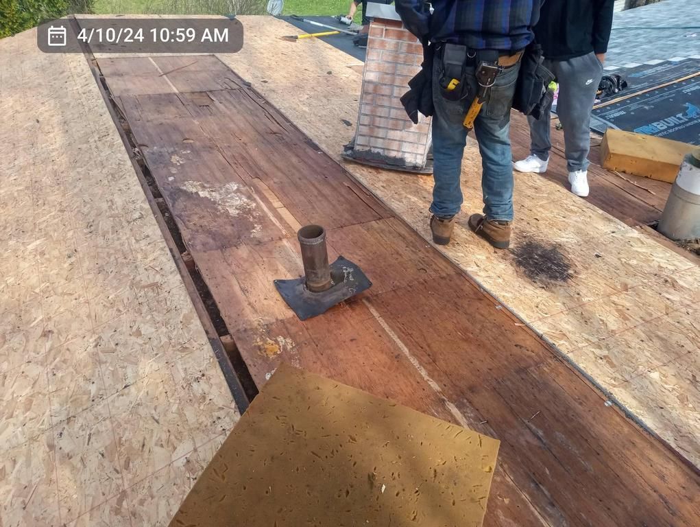 Construction workers on a residential roof during a renovation, featuring exposed wooden decking and a plumbing vent.