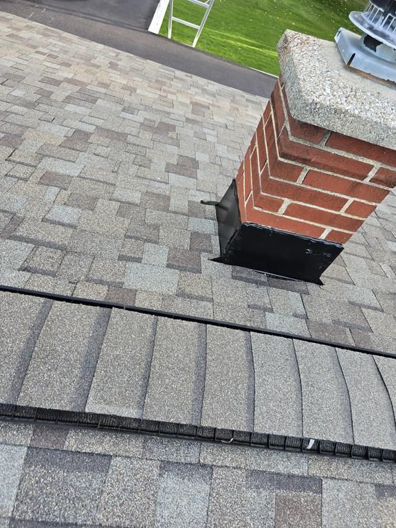 A red brick chimney with black metal flashing installed on a gray-toned asphalt shingle roof.