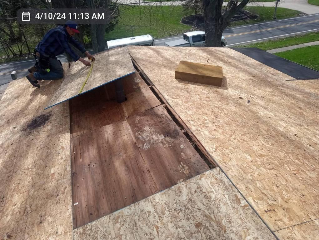 A person installing plywood sheeting onto a roof frame on a sunny day.