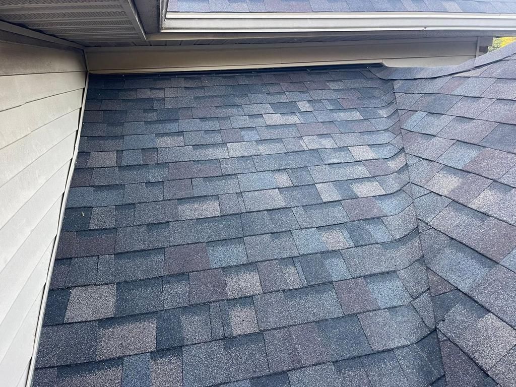 A close-up of a residential asphalt shingle roof where it meets a siding wall, showing the shingles and transition area.