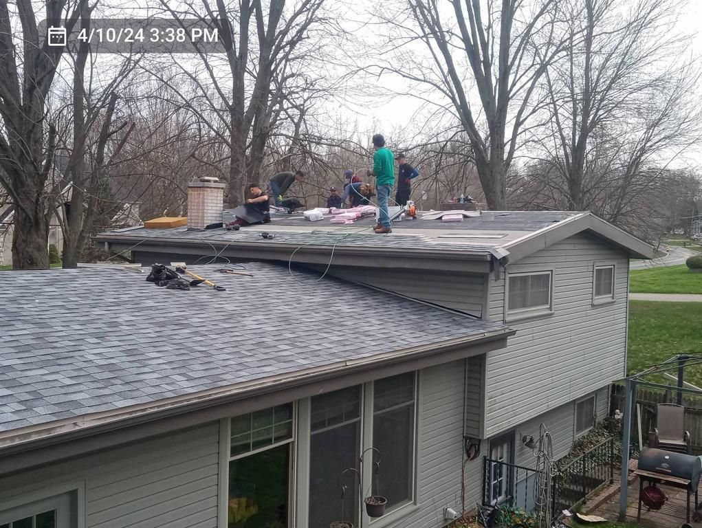 Workers installing roofing materials on the flat upper section of a split-level home on a cloudy day.