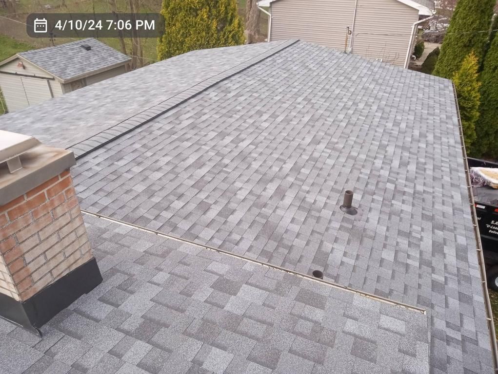 A high-angle view of a grey shingled roof with a brick chimney and plumbing vent.