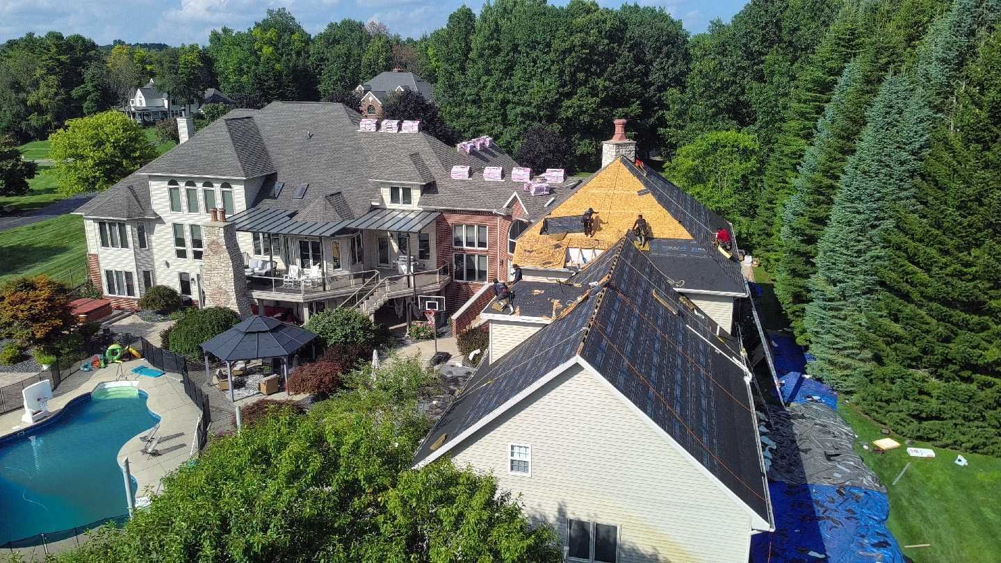 Aerial view of a large residential house with a pool, showing sections of the roof under construction or repair.