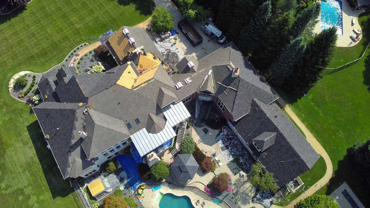 Aerial view of a large multi-roof residential estate with two swimming pools, surrounded by green lawns and trees.