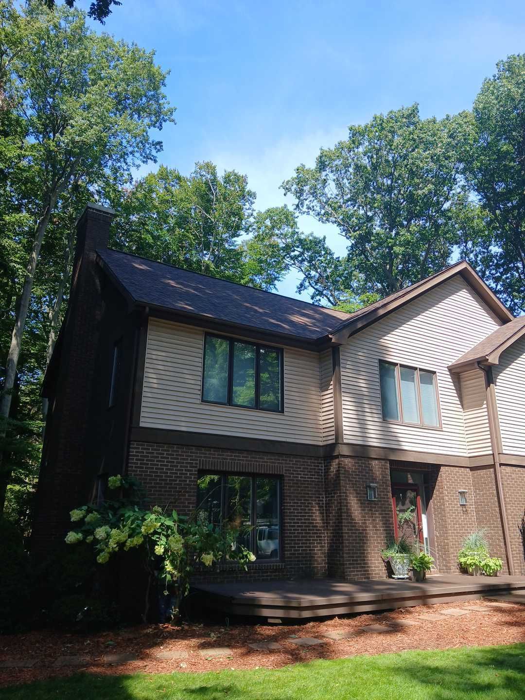 A two-story house with brick siding on the bottom and light tan horizontal siding on top, surrounded by trees.