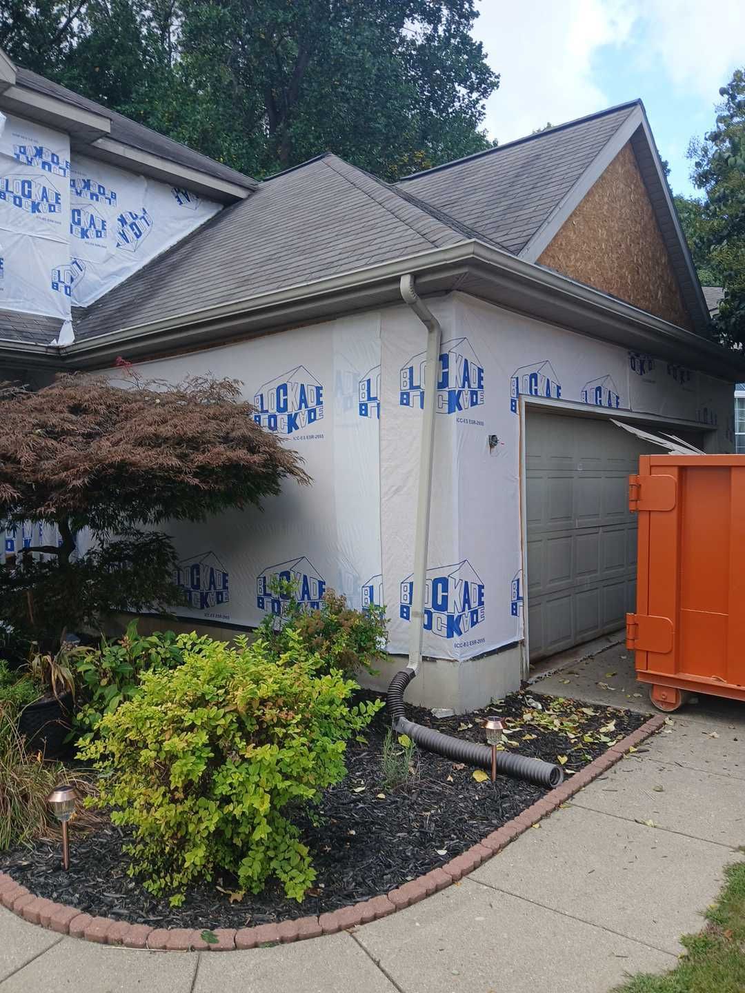 The exterior of a house under renovation with blue weather-resistant barrier panels and an orange dumpster nearby.