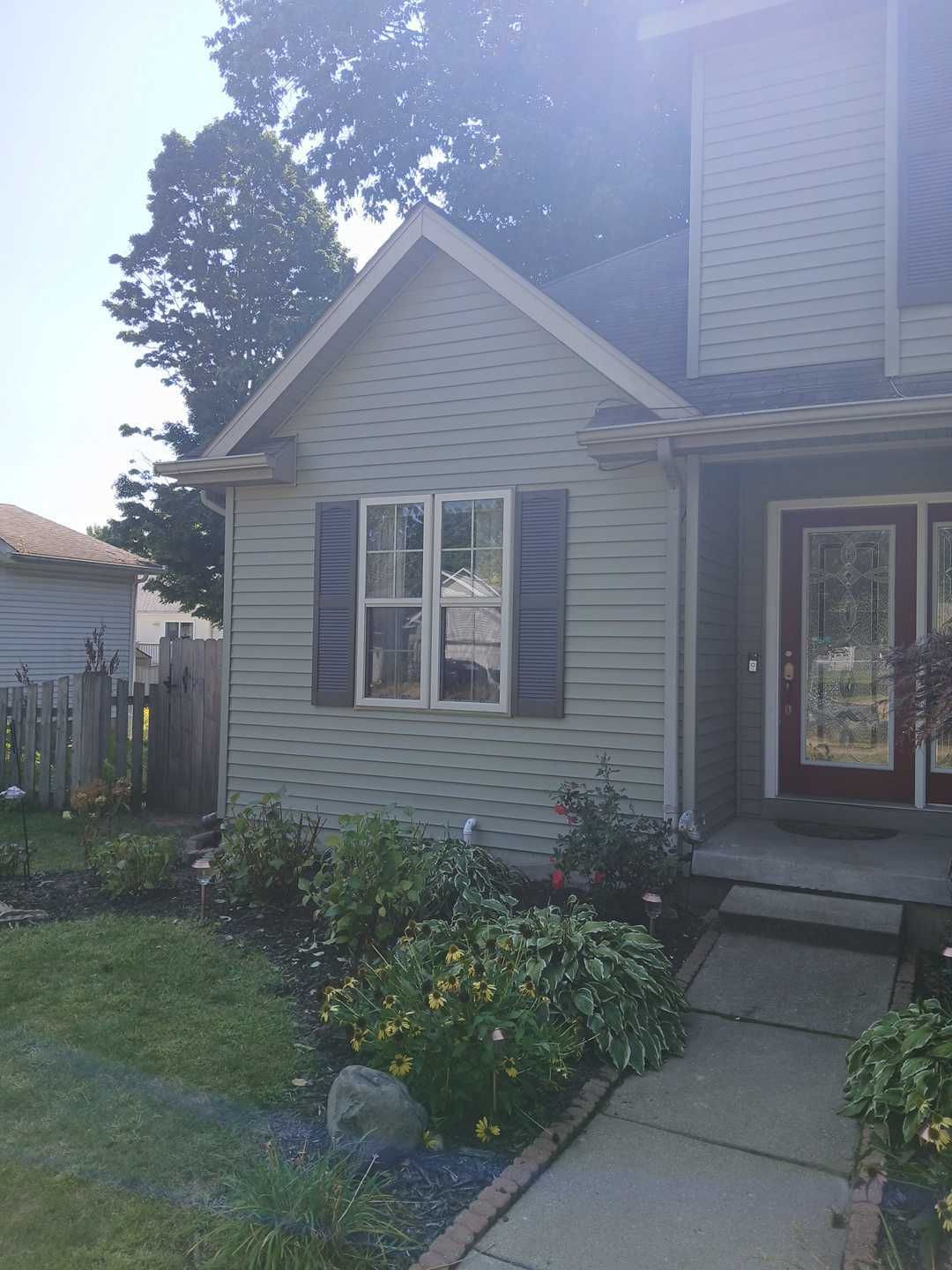 A light gray-sided suburban home exterior with a red front door, a window with dark shutters, and a front walkway.
