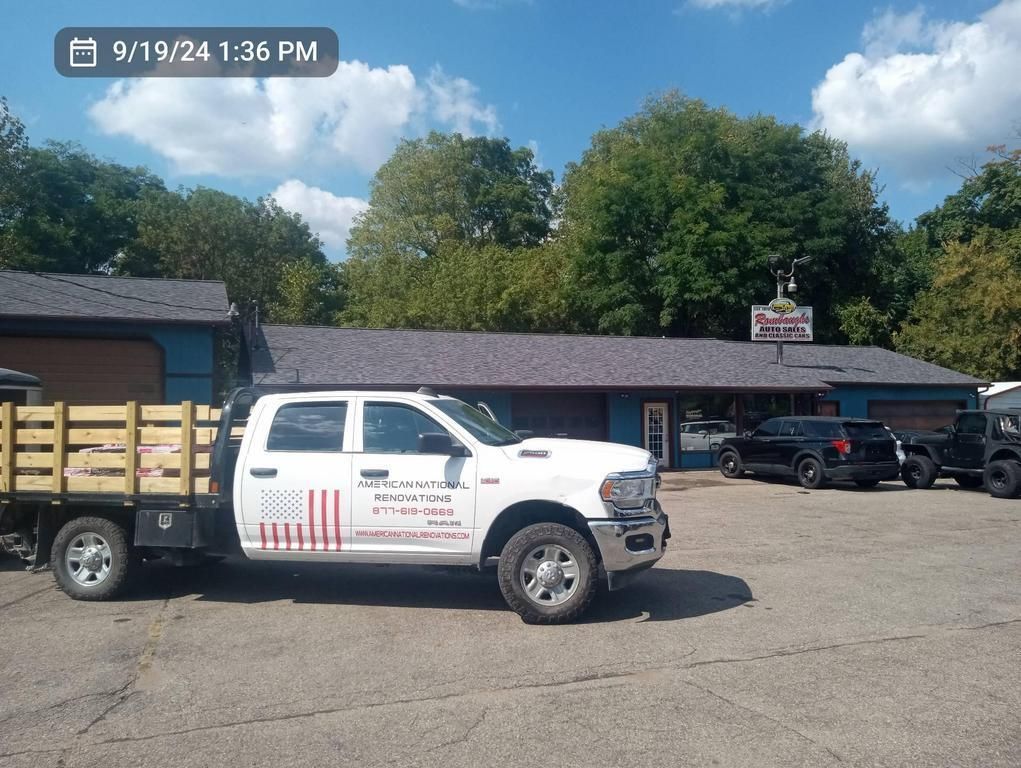 A white flatbed truck parked in front of a building with a “Sun-Lite” sign under a blue sky.