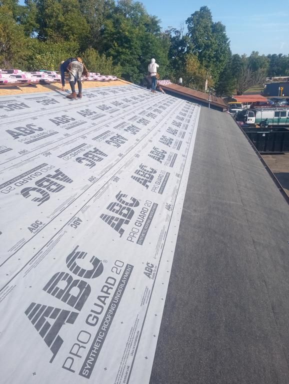 Construction workers installing synthetic roofing underlayment labeled 