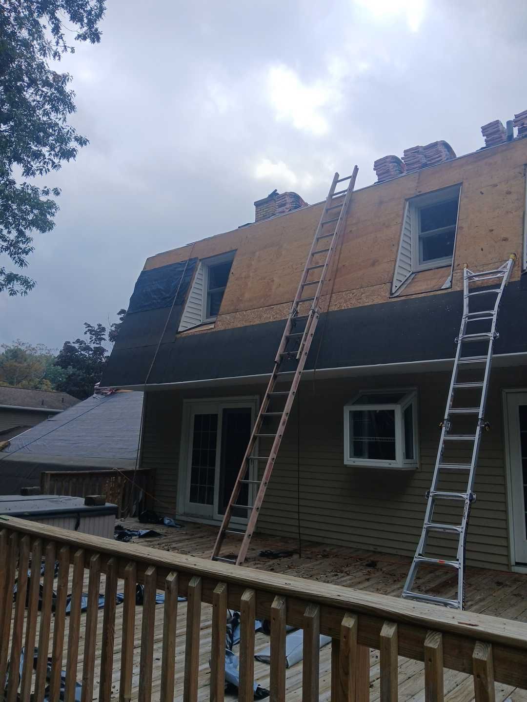 Exterior of a house under renovation with two tall ladders leaning against the siding and a partially shingled roof.