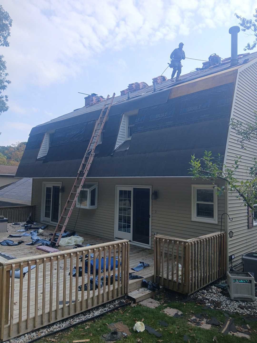 A construction worker stands on the roof of a two-story home during a shingle replacement project.