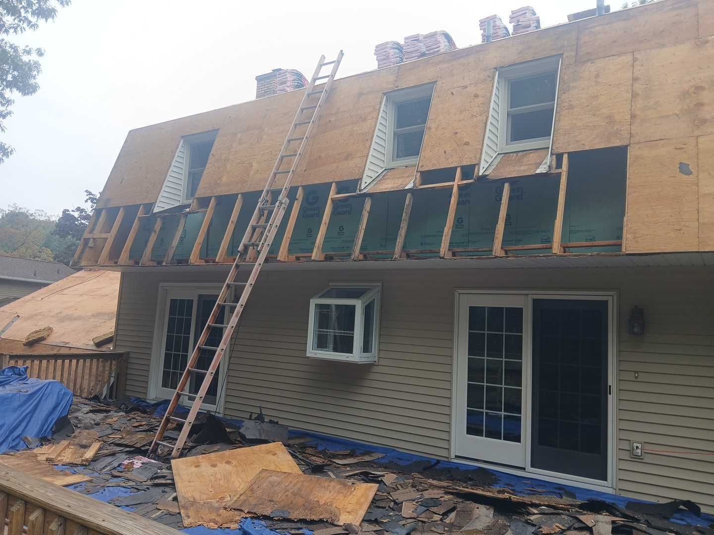 A house undergoing roof repairs with a ladder leaning against the exterior, surrounded by scattered roofing debris.