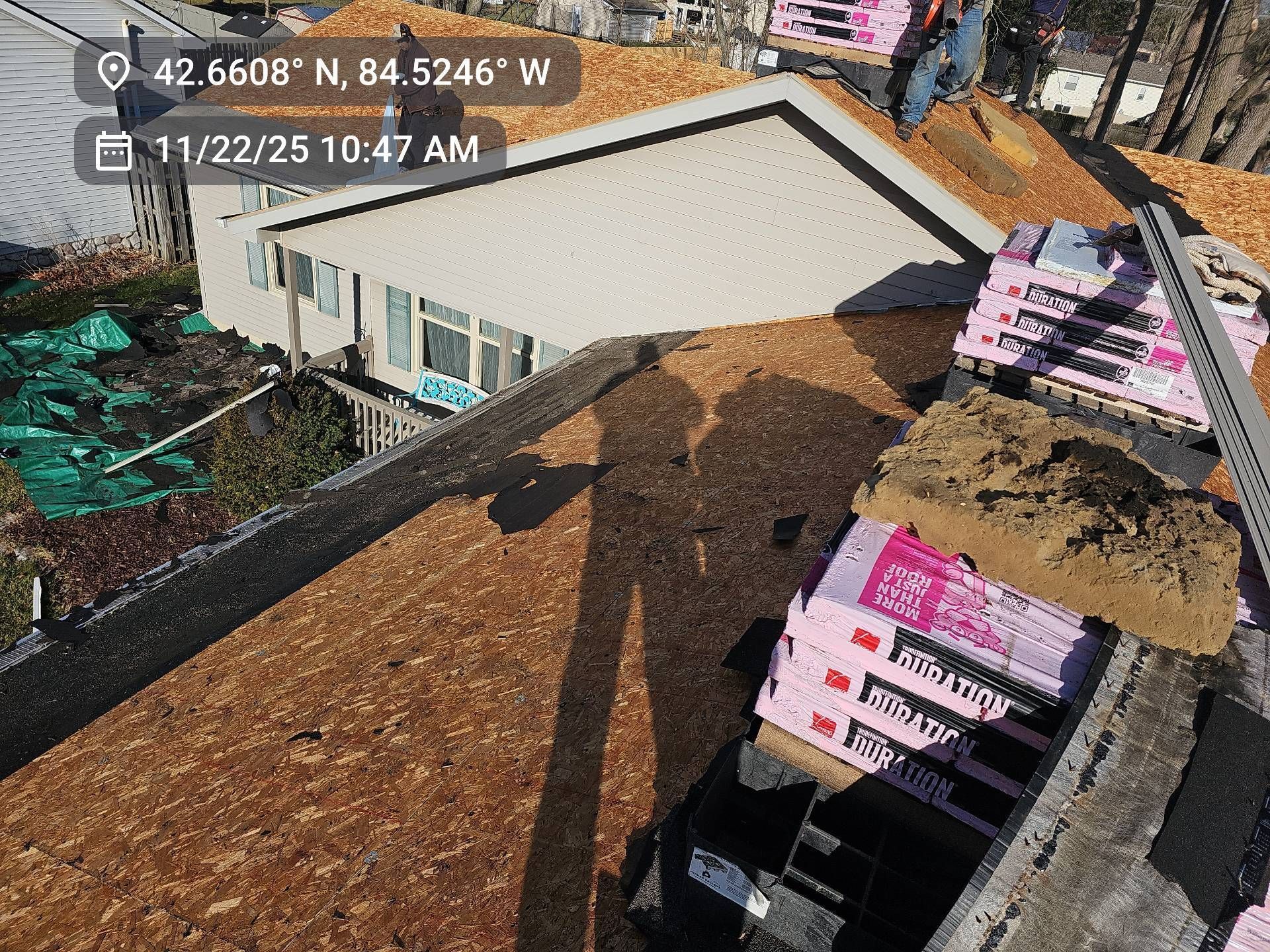 A person on a roof during construction, with stacks of pink insulation boards nearby on a sunny day.