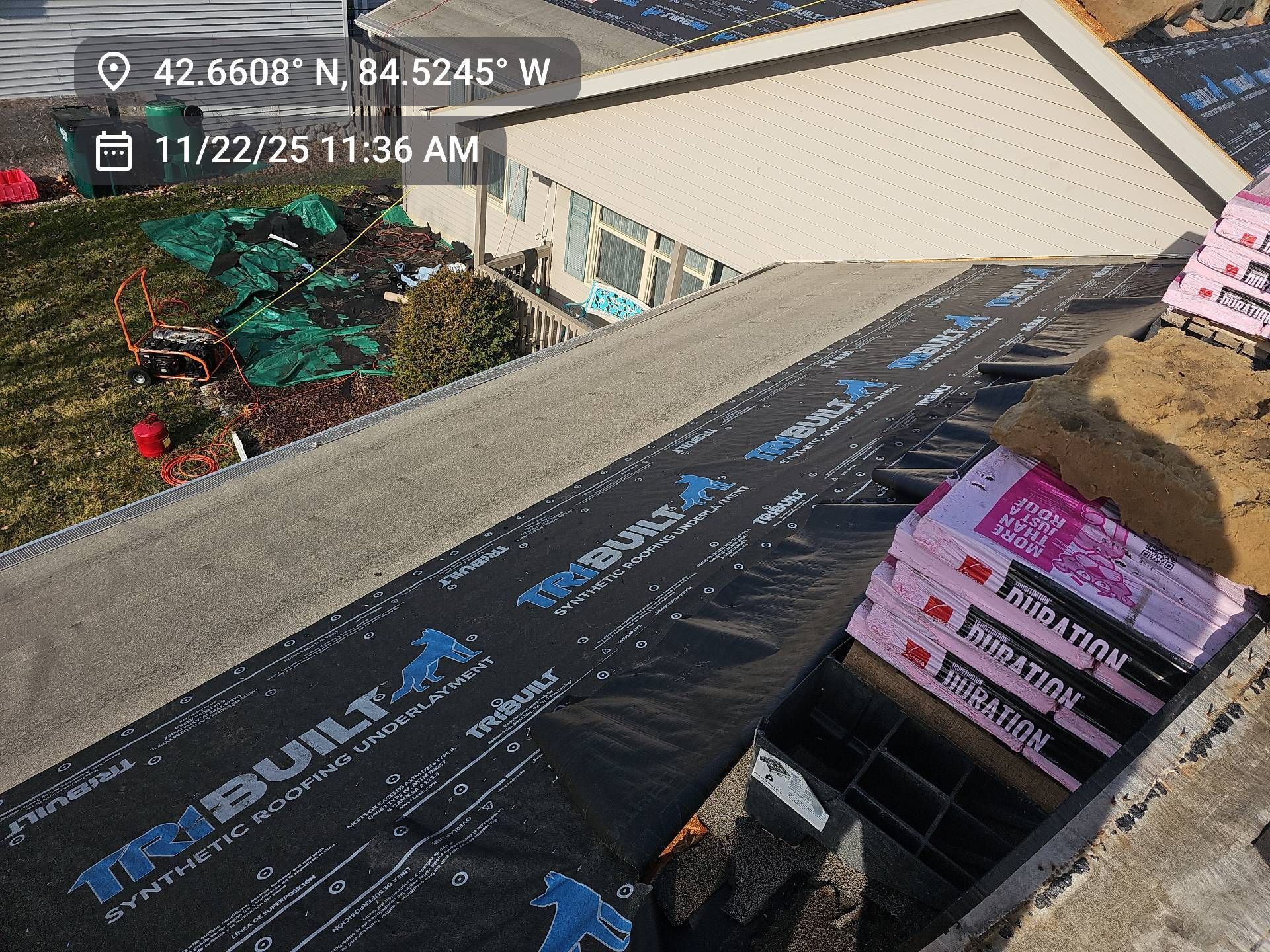 A roof under construction with black synthetic underlayment and a stack of pink roofing shingles.