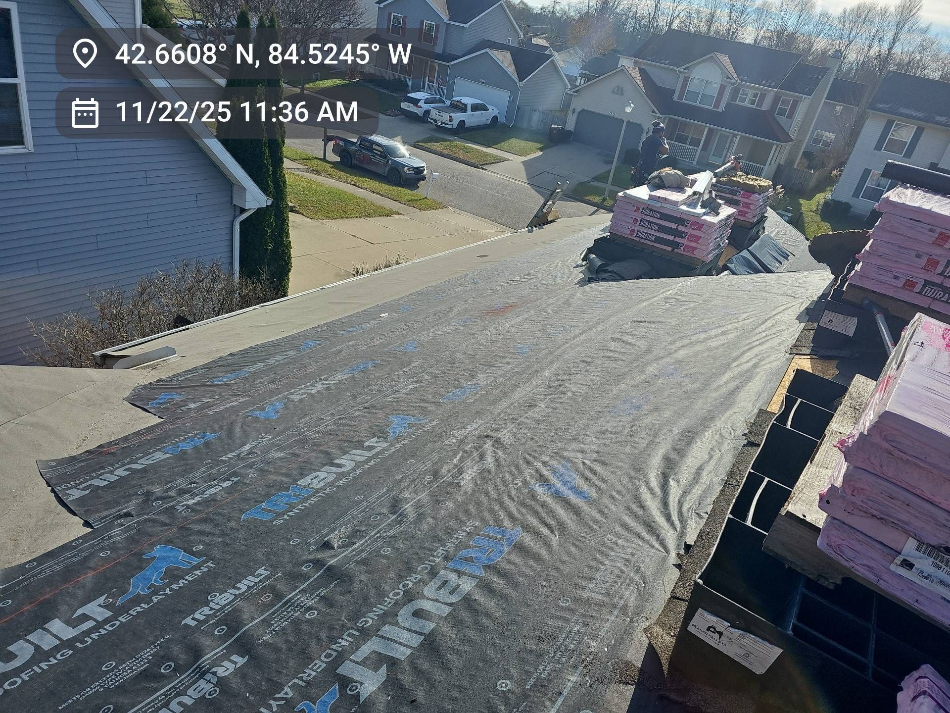 A view from a residential roof under construction, showing black underlayment laid out with stacks of pink insulation.