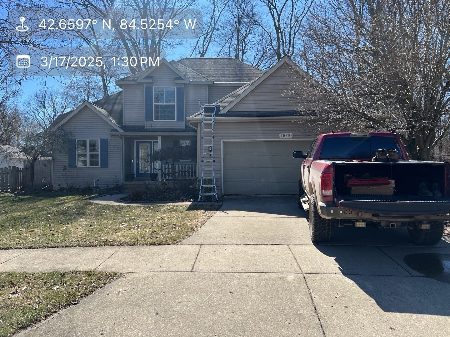 A two-story tan house with a garage and a red pickup truck parked in the driveway on a sunny day.