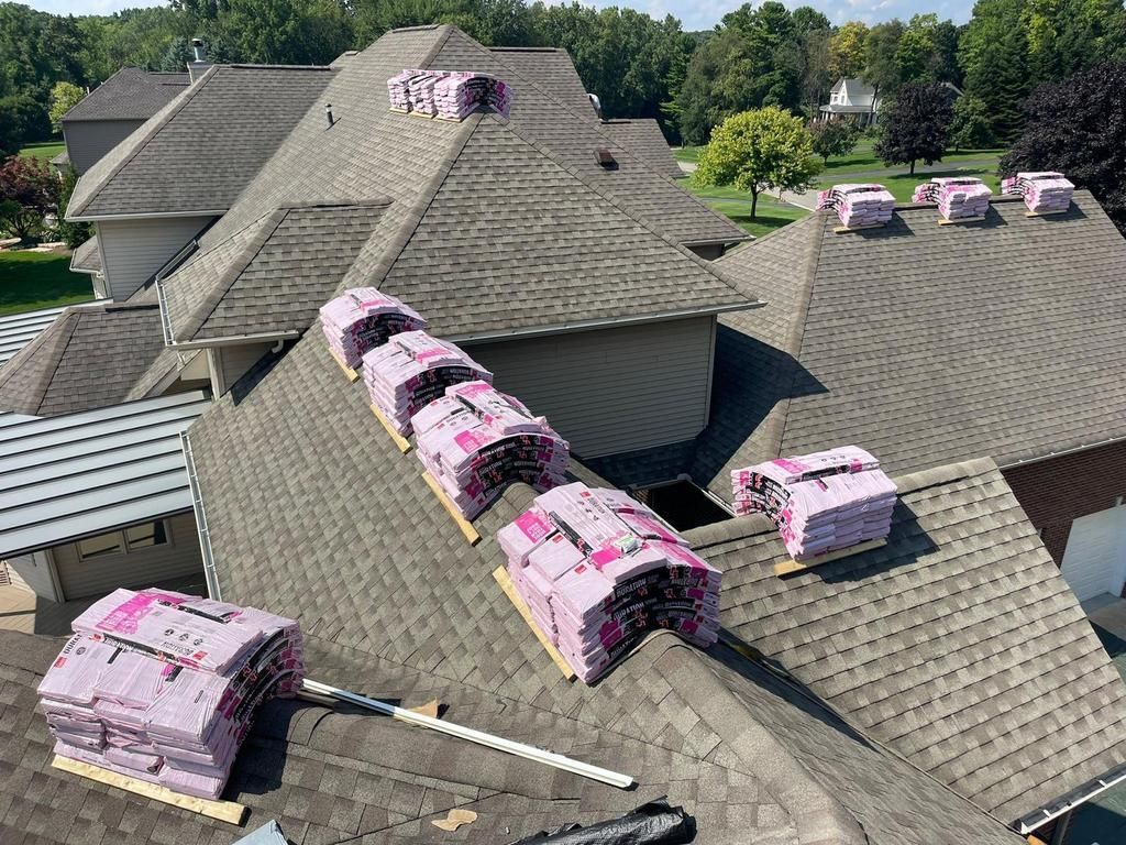 Stacks of pink asphalt roofing shingles arranged on the slopes of a shingled roof awaiting installation.