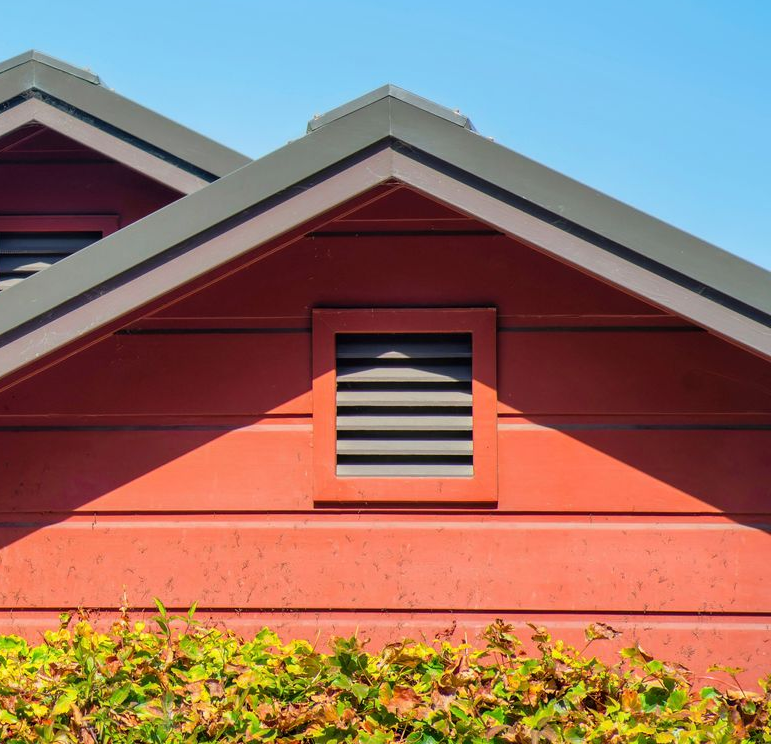 The peaks of three red, triangular roofs are set against a clear blue sky, partially obscured by green tree branches.