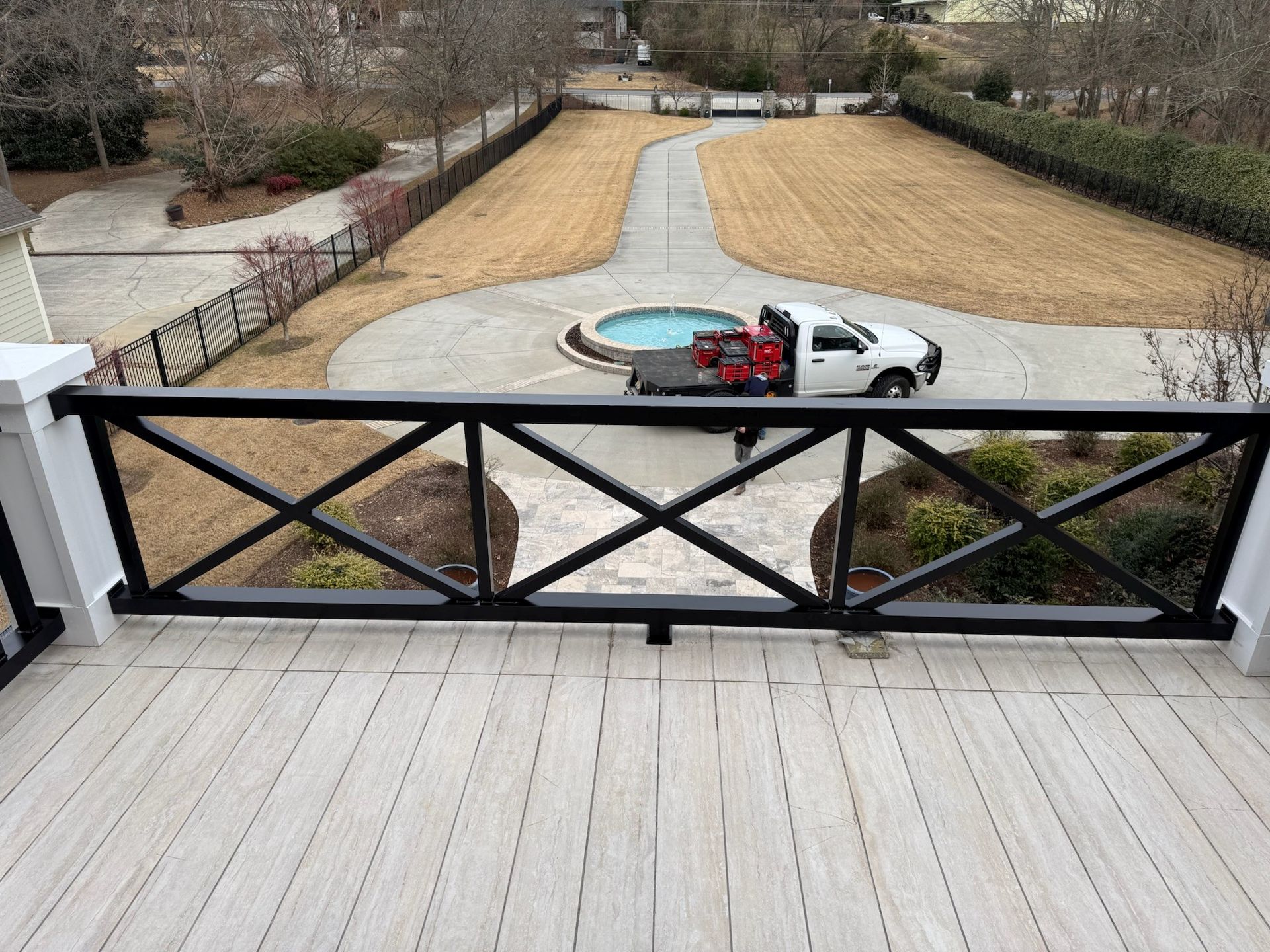 White pickup truck on a driveway beside a round fountain, viewed from a porch with a black railing.
