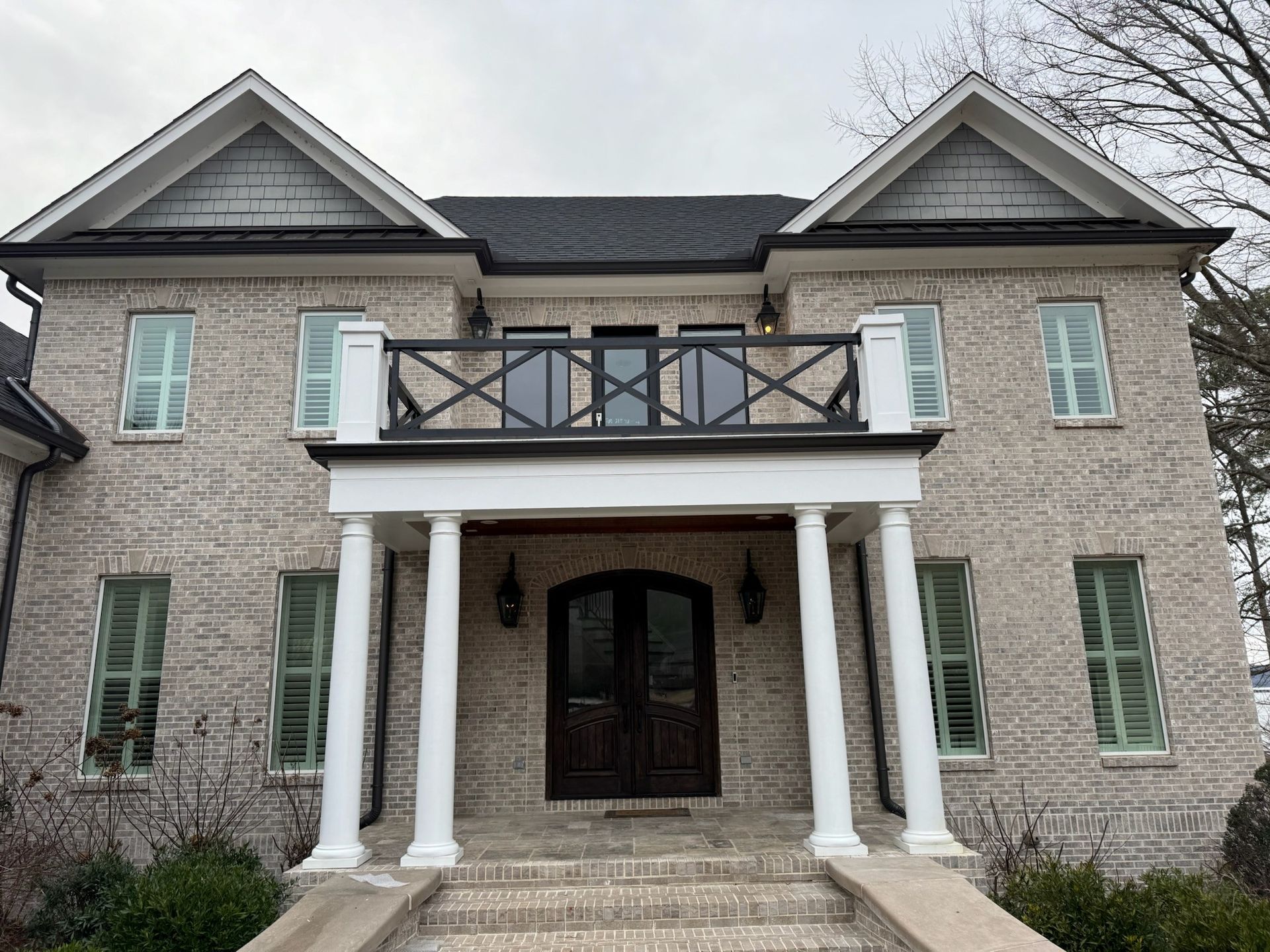 Stone house with white columns, dark front doors, and a black balcony above the entry