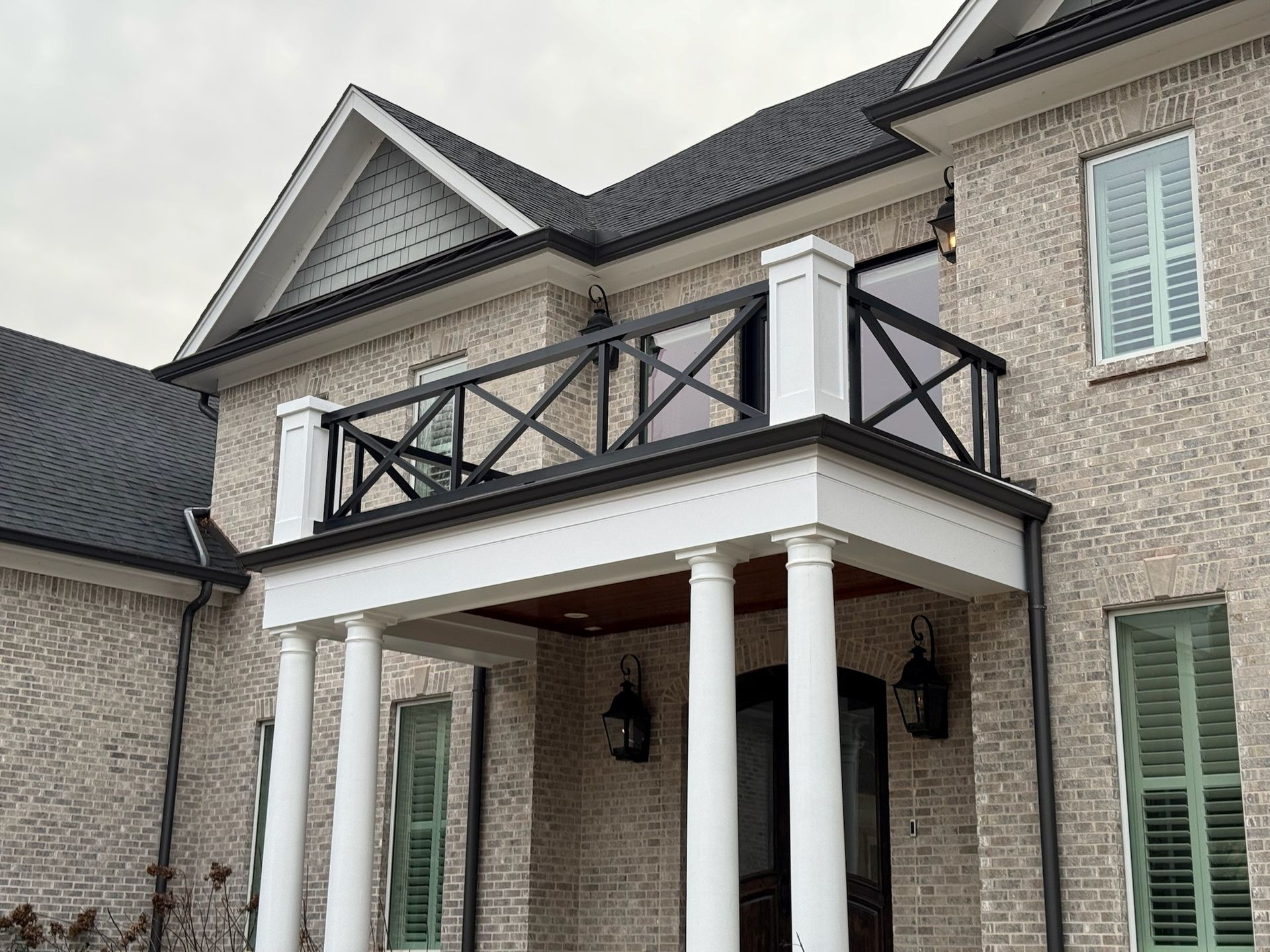 Front porch of a gray brick house with white columns, black railings, and dormer windows