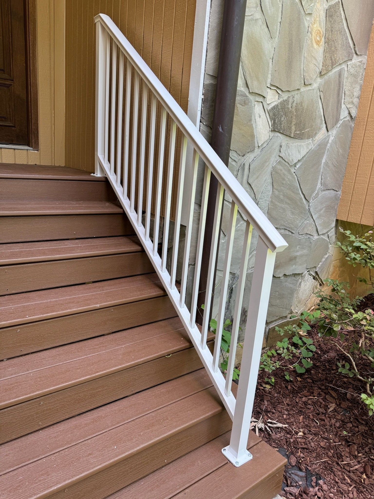 White metal handrail beside outdoor stairs leading to a wooden door.