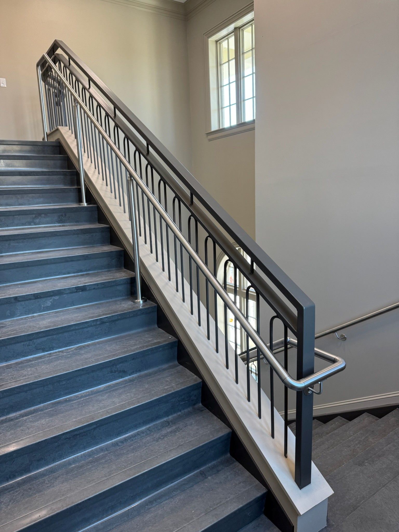 Indoor staircase with gray steps, black handrails, and a small window on the landing