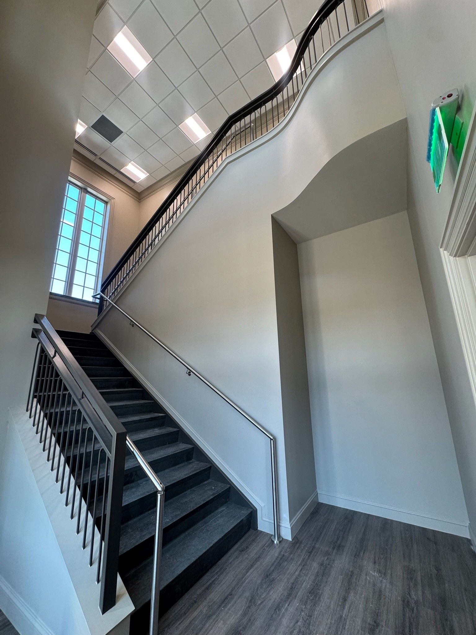 Modern indoor stairwell with black railings, gray floors, and a white arched wall.