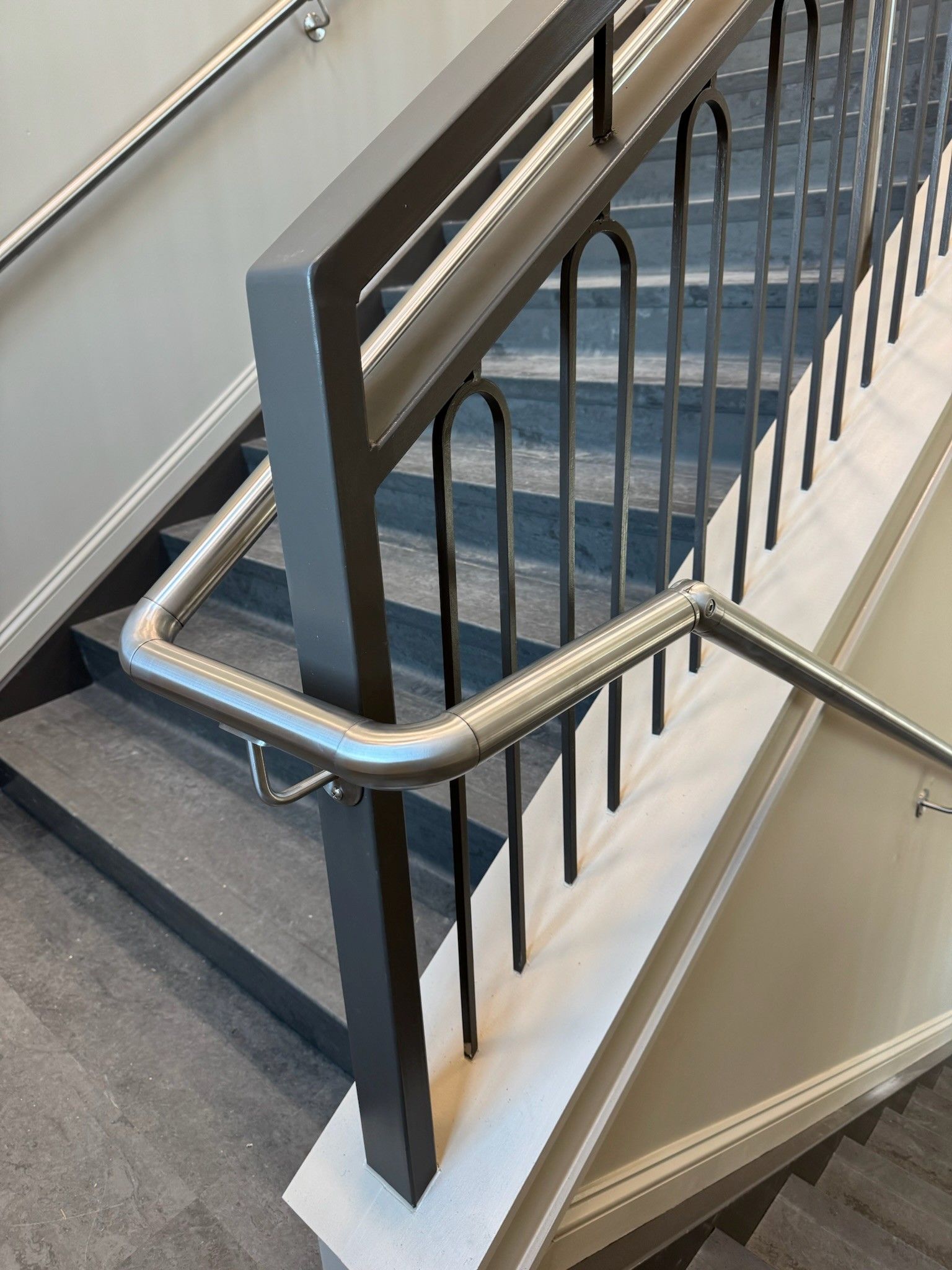 Stairwell with blue carpeted steps, metal handrails, and black balusters along a landing.