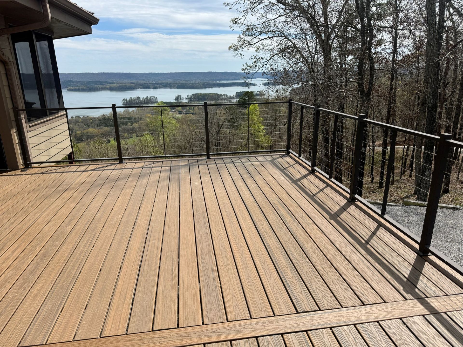 Wooden deck with black railing overlooking a lake and distant shoreline on a clear day