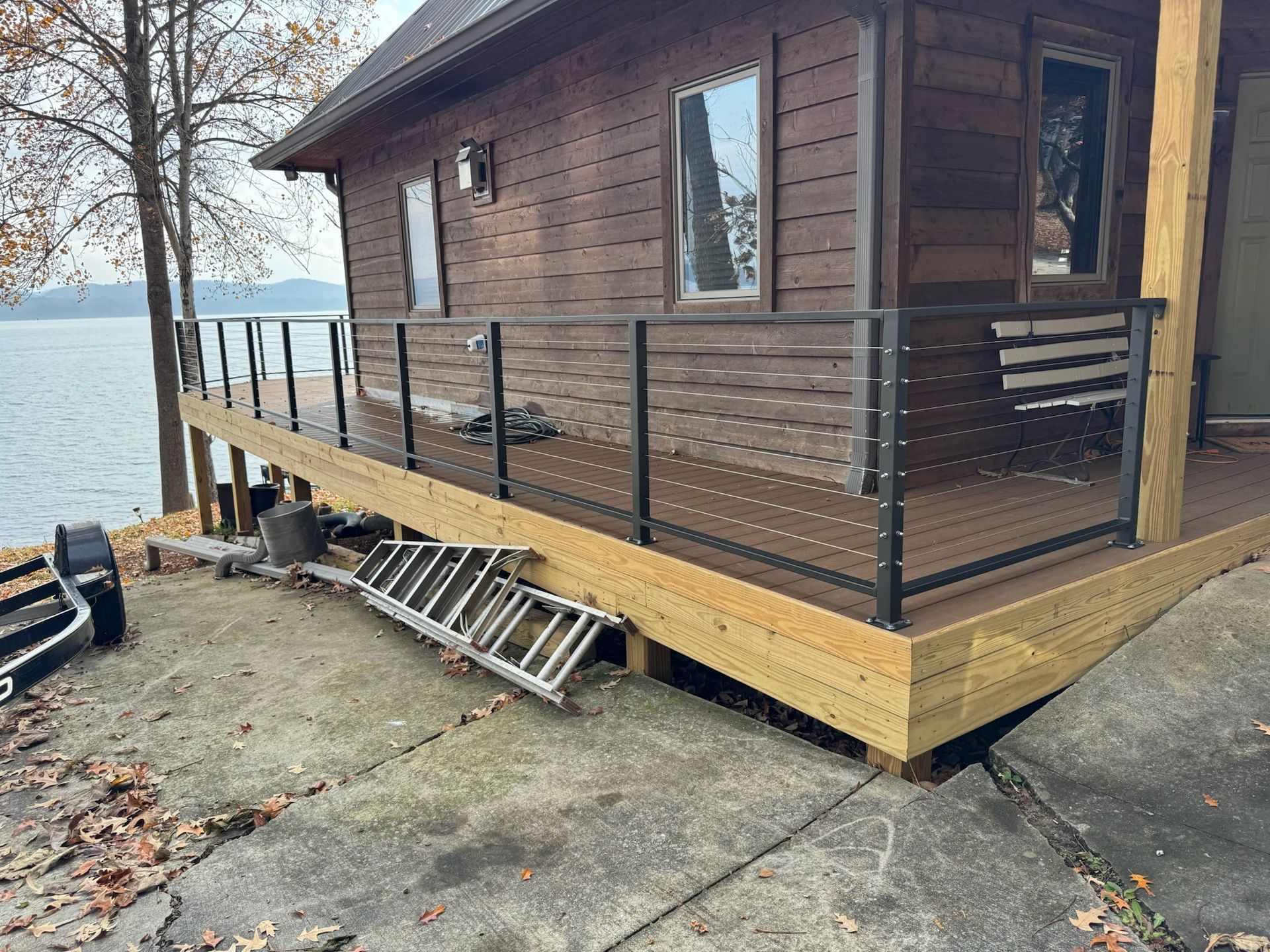 Small brown lakeside cabin with porch, wheelchair ramp, and a leaning ladder outside