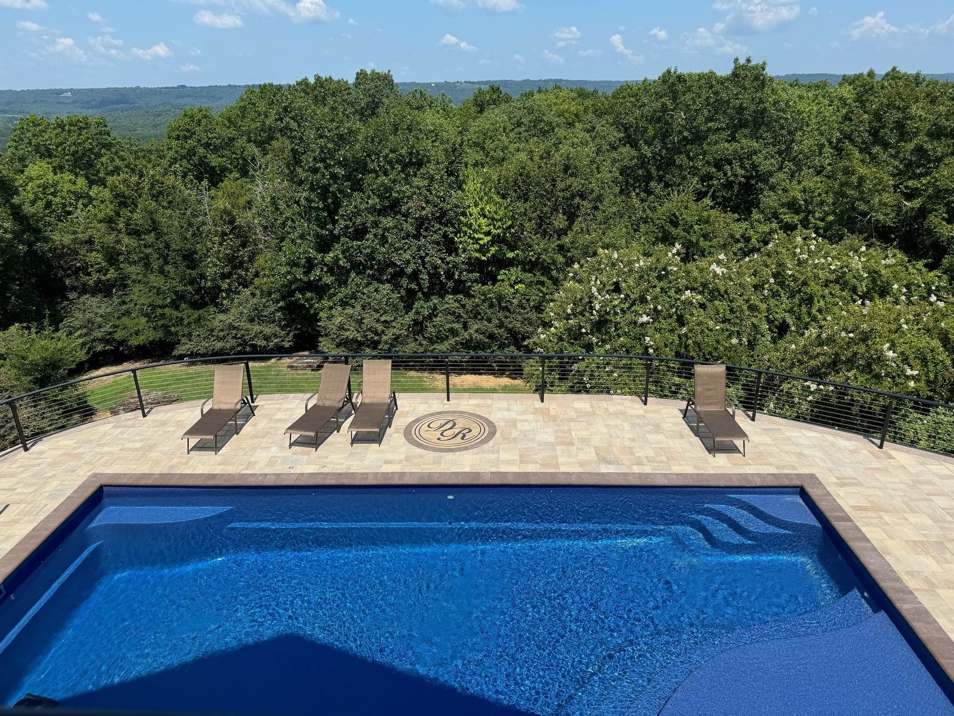Backyard pool with lounge chairs, stone deck, and lush trees beyond