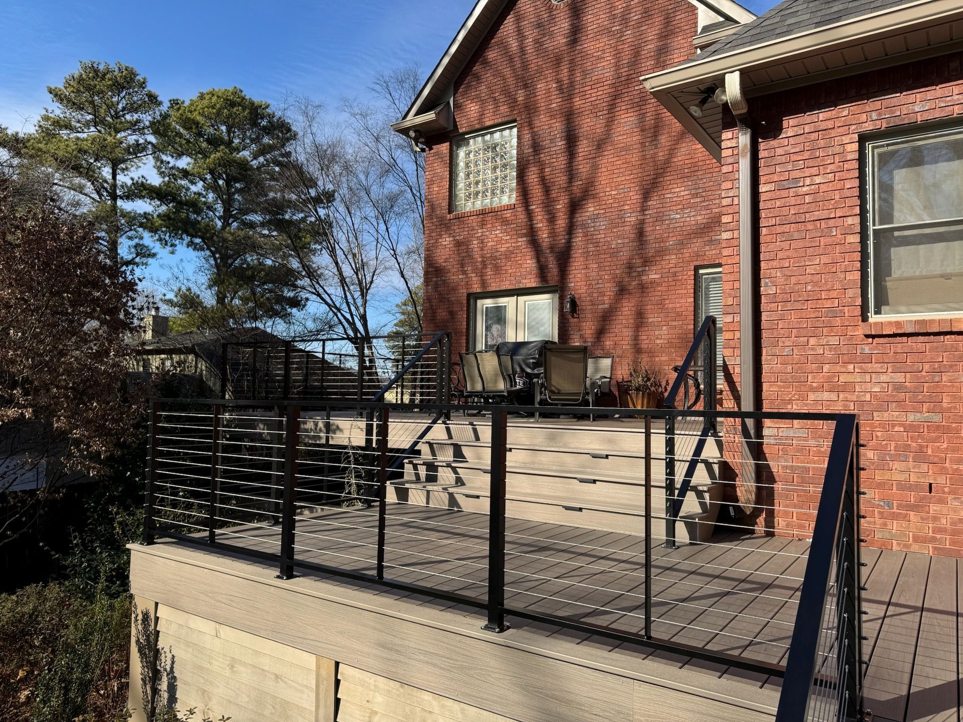 Brick house patio with black railing, steps, outdoor chairs, and a sunny yard beyond